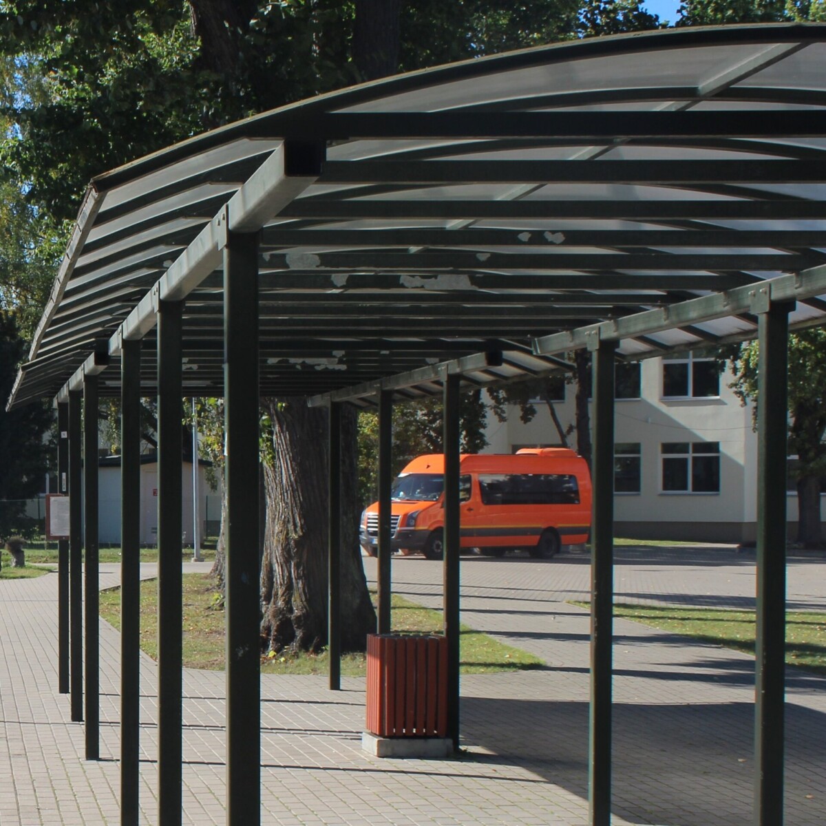Skolēnu autobusa nojume un oranžs skolēnu autobuss